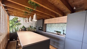 Una cocina moderna con una isla grande, vigas de techo de madera y un salpicadero con un mural tropical.