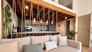 Una sala de estar moderna con un sofá color beige, una cocina al fondo y un techo de madera con vigas a la vista.