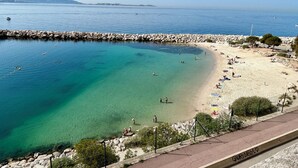 Una playa costera con aguas cristalinas, un espigón rocoso y un paseo marítimo pavimentado.