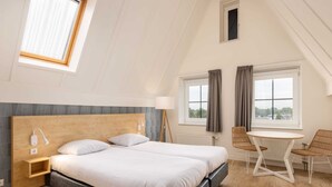 A bedroom with a large bed, bedside tables, a lamp, and a view of the city through windows. - Comfortable Hotel Room in Center of Volendam (Volendam)