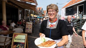 A person holding a plate with food, standing in a street with outdoor seating and a menu board visible. - Comfortable Hotel Room in Center of Volendam (Volendam)