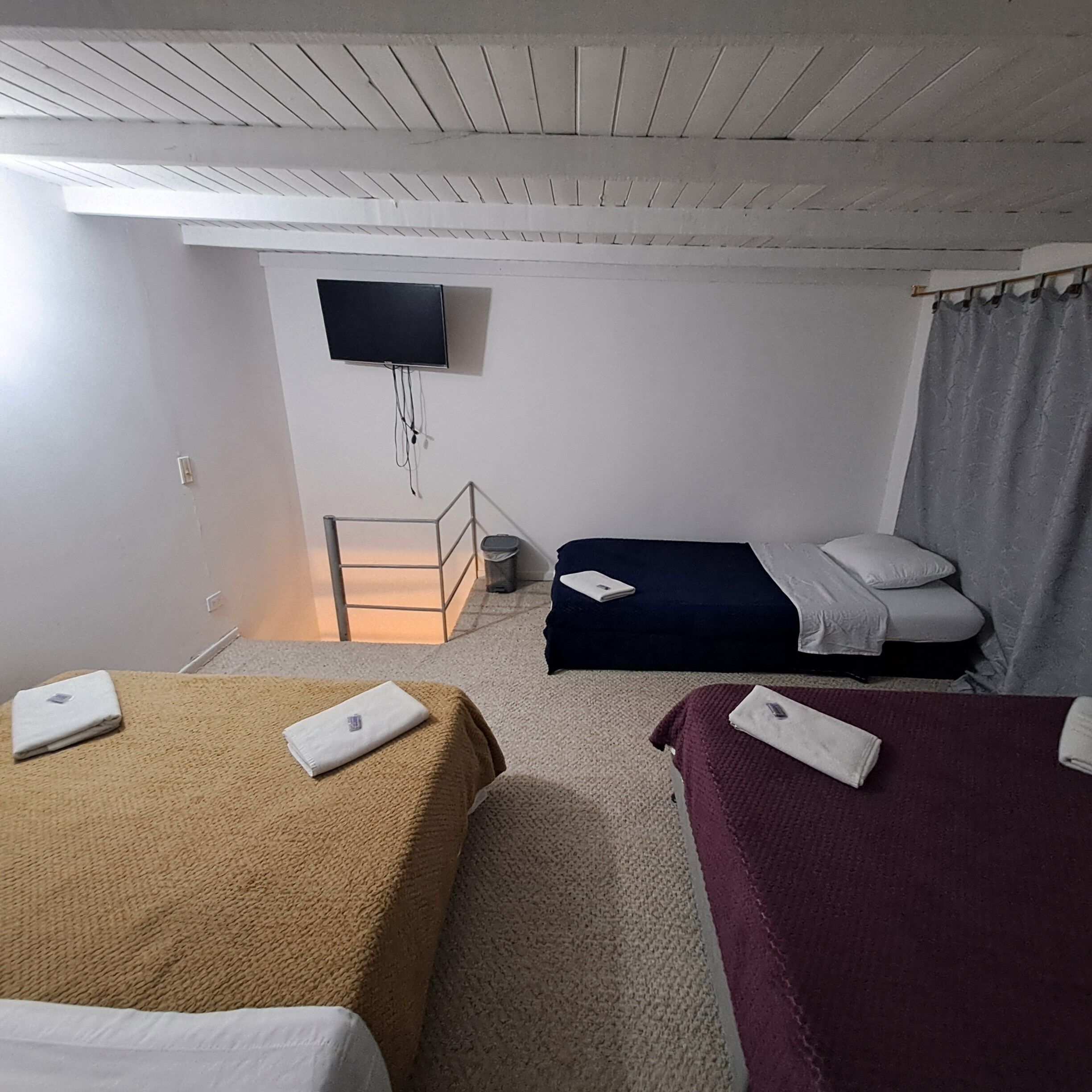 Habitación de hotel con dos camas, un televisor montado en la pared y una mesita de noche con lámpara.