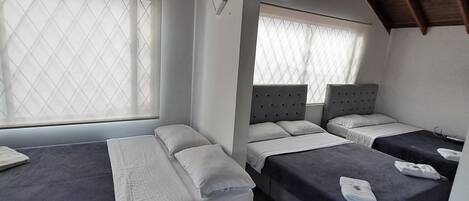 A room with two beds, a window with a diamond-patterned blind, and wooden ceiling beams.