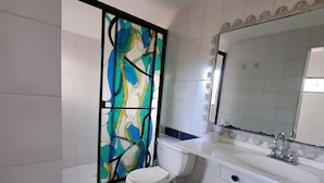 A bathroom with a white toilet, a sink with a mirror, and a trash bin. - Fortaleza Diosa Chia (Chia)