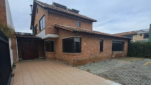 A two-story brick house with a tiled patio, a gated entrance, and a small garden area. - Fortaleza Diosa Chia (Chia)