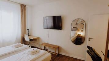 Una habitación de hotel con una cama, un escritorio, un televisor y un espejo.