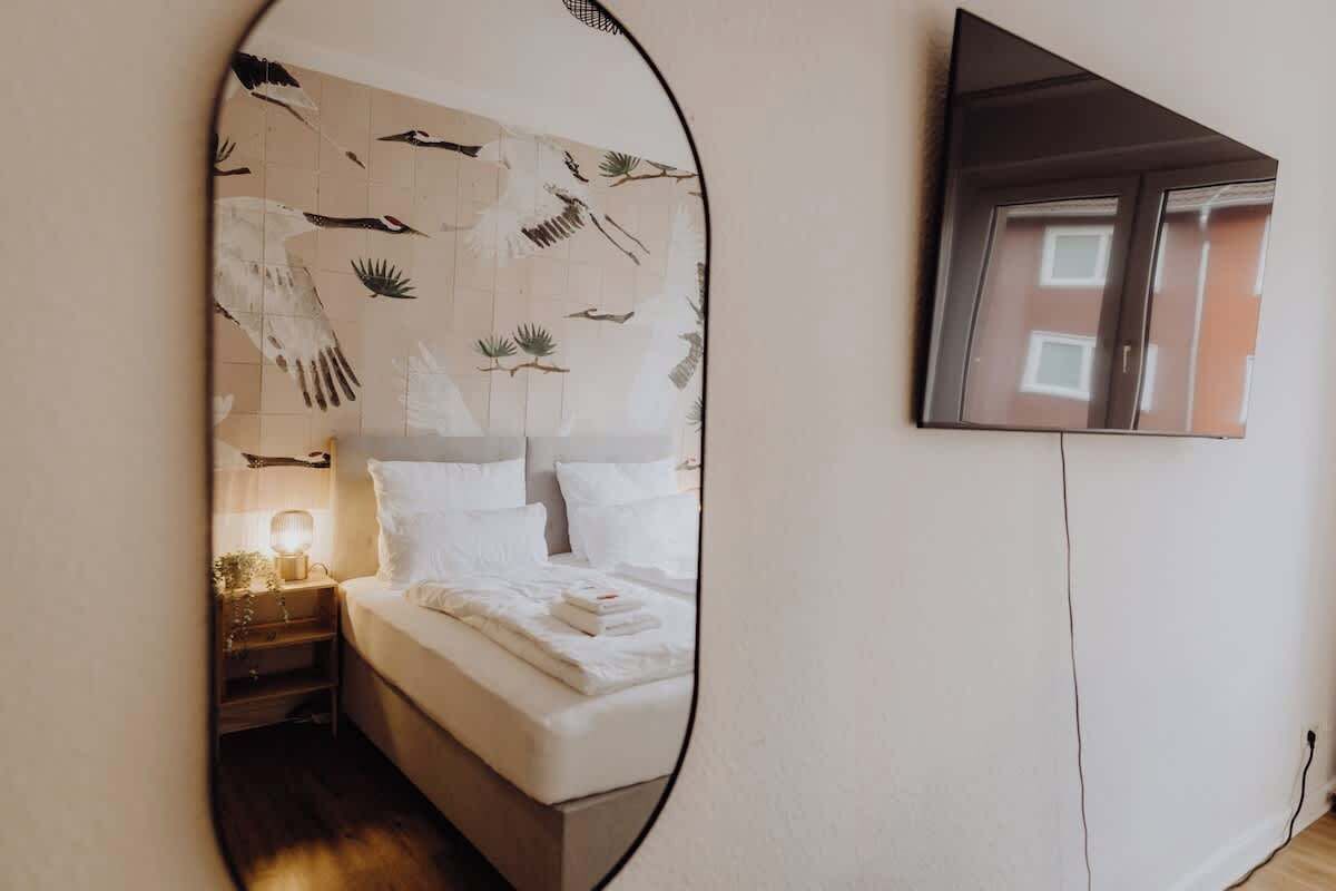 Une chambre à coucher avec un lit, une table de chevet, une lampe et un miroir qui reflète la pièce.