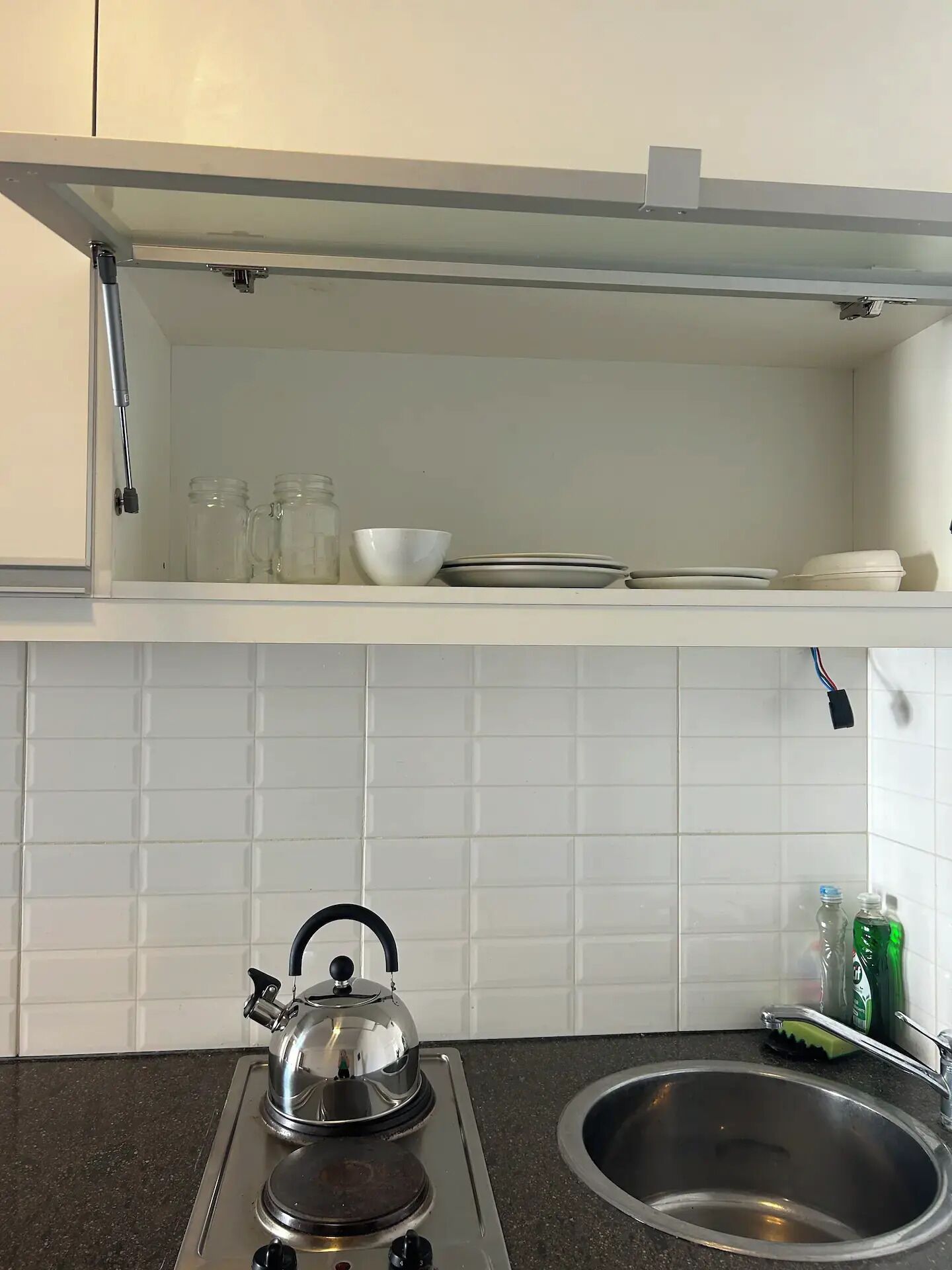 Una cocina con estufa, lavaplatos y salpicadero de azulejos blancos.