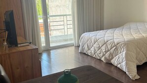 Ein Hotelzimmer mit Bett, einem Holztisch, einer Klimaanlage und Blick durch eine Glastür.