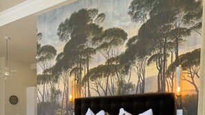 Un dormitorio con una cama grande, un mural con motivos forestales en la pared, una lámpara de araña moderna y suelo de madera.