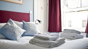 A neatly made bed with folded white towels, a blue and white patterned pillow, and a red curtain. - The Red Lion (Knighton)