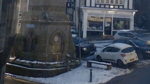 A historic clock tower with a traditional clock face, a Tudor-style building with 'The Headmaster' sign, and a snow-covered street. - The Red Lion (Knighton)