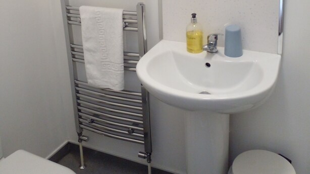 Ein Badezimmer mit weißem Waschbecken, Spiegel, Handtuchhalter und Toilette.