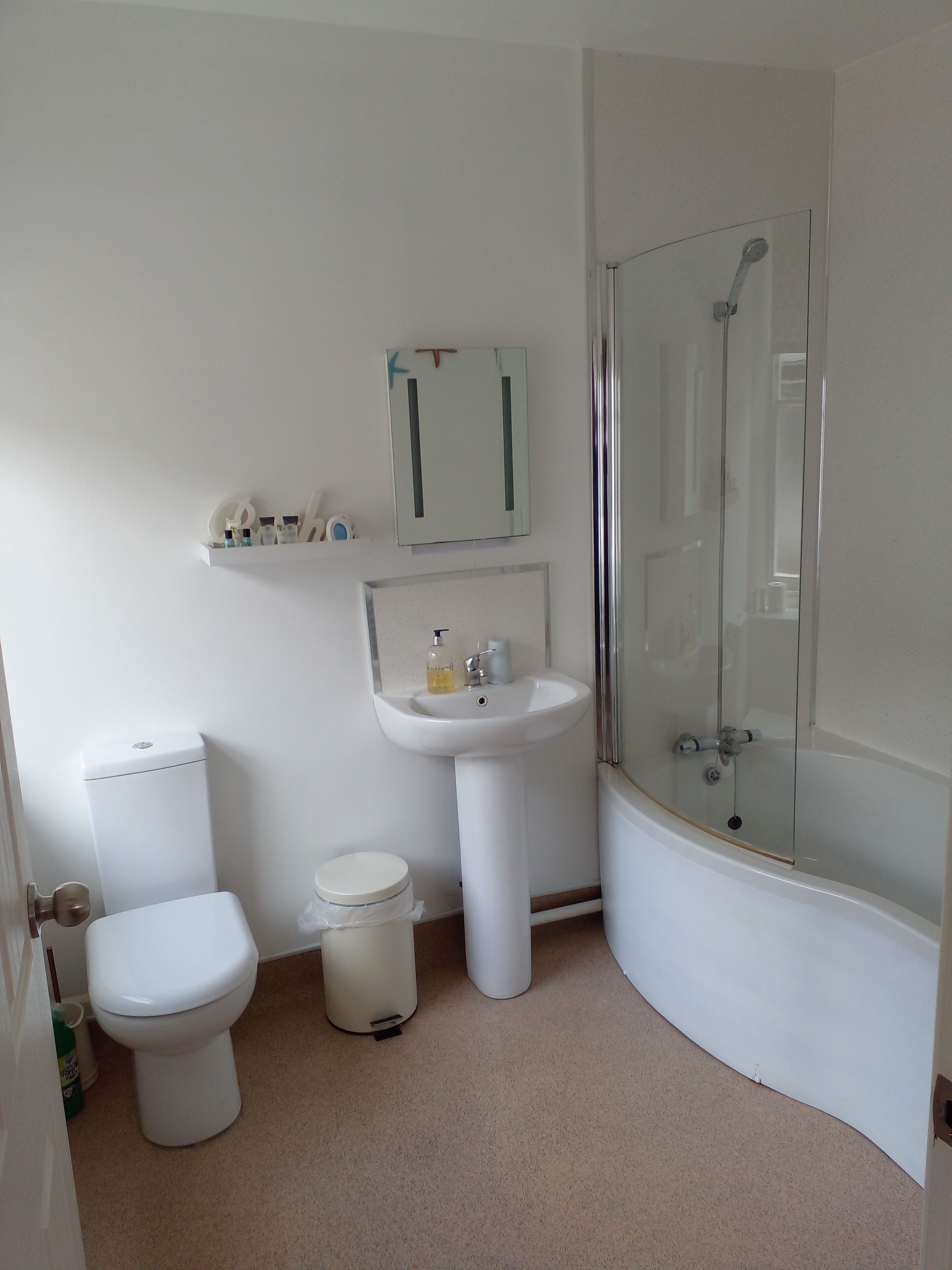 Un baño con inodoro, lavamanos y ducha con mampara de vidrio.