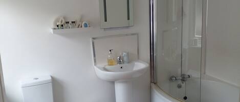 Un baño con inodoro, lavamanos y ducha con mampara de vidrio.