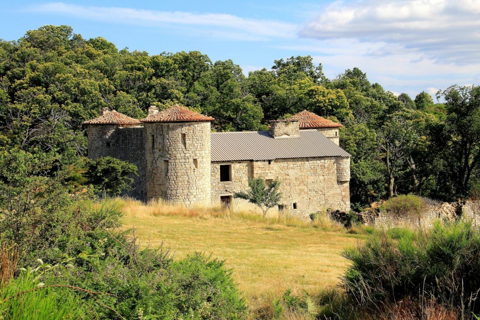 Un edificio de piedra con techo de tejas, rodeado de un bosque frondoso.