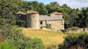 Un edificio de piedra con techo de tejas, rodeado de árboles y césped frondosos.
