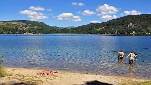 Un lago con barcos, una playa de arena y gente en el agua.