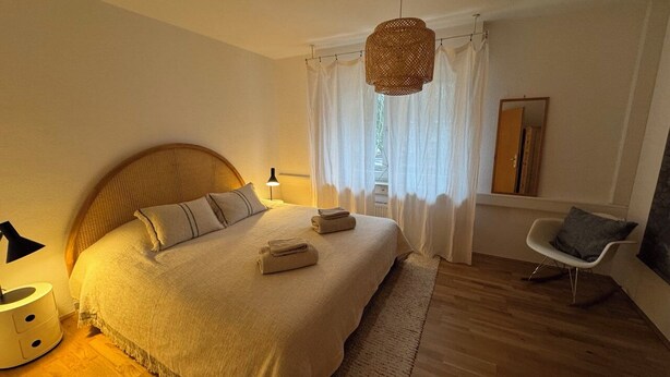 A bedroom with a large bed, a bedside lamp, a chair, and a hanging light fixture. - Spacious vacation apartment in Leverkusen-Opladen, quiet but centrally located (Leverkusen)