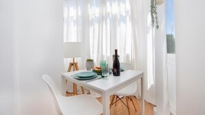 Een lichte kamer met een witte tafel gedekt voor twee personen, een fles wijn en een kleine plant op de vensterbank.