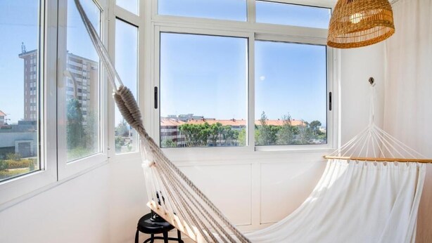 Een kamer met een groot raam, een hangmat en een rieten lamp.