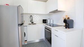 Een moderne keuken met witte kasten, een roestvrijstalen koelkast, een magnetron, een koffiezetapparaat en een vaatwasser.