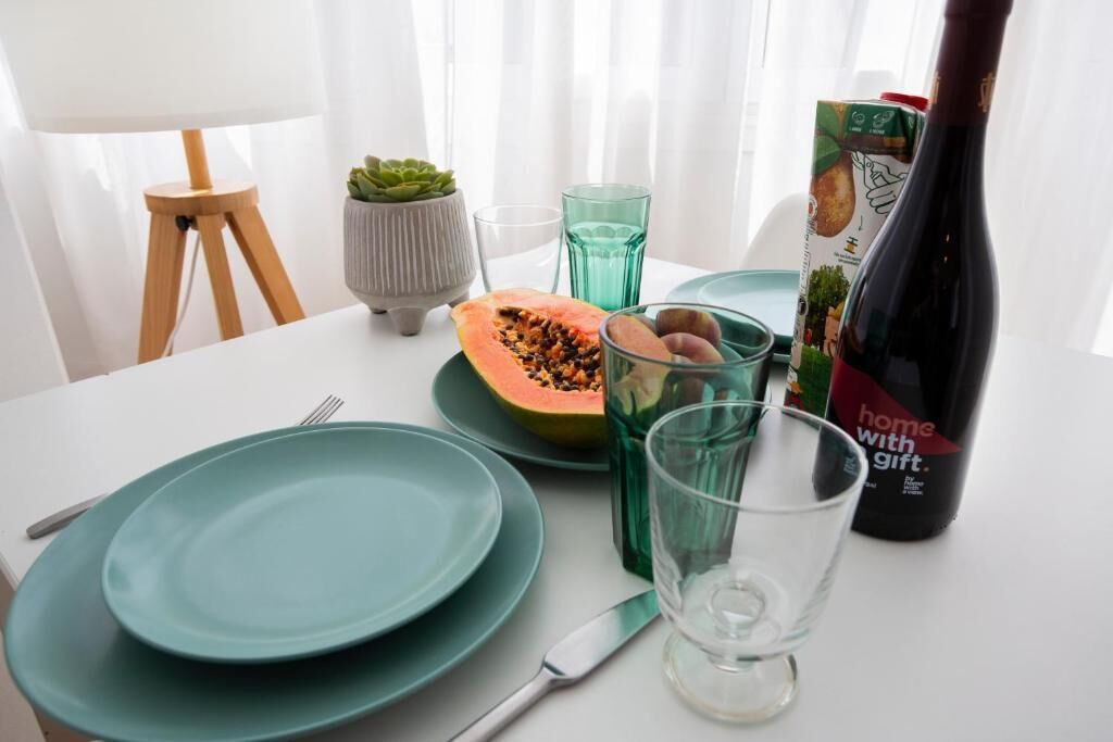 Pöydällä on vihreitä lautasia, puoliksi leikattu papaija, vihreä lasi, mehupullo ja pieni ruukkukasvi.