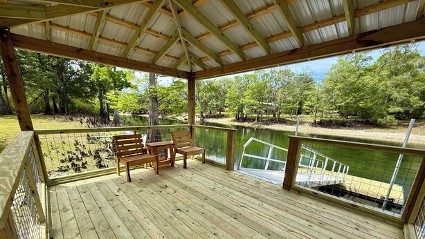Une terrasse en bois avec une rambarde en métal, donnant sur une étendue d’eau et entourée d’arbres.