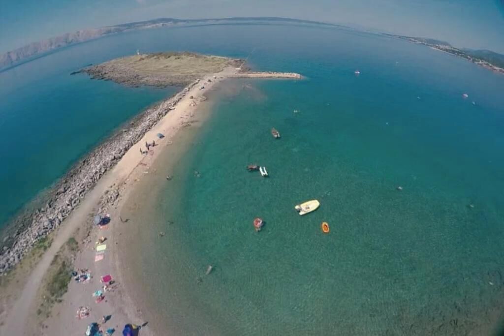 An aerial view of a coastal area with a sandy beach, clear blue water, and several boats.