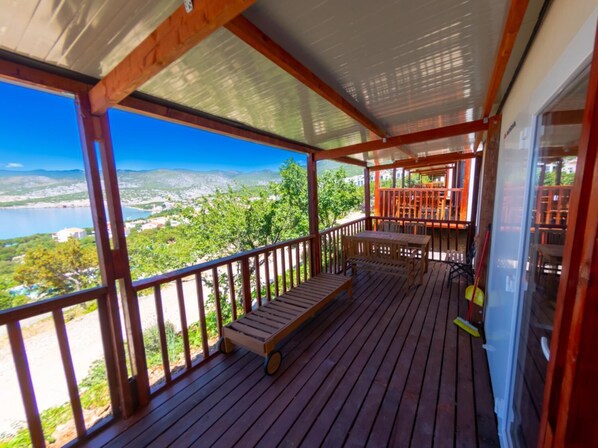 A wooden deck with a bench, a table, and chairs, overlooking a scenic view of a lake and mountains.