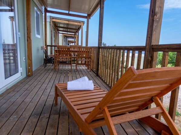 A wooden deck with a covered seating area, a wooden bench with a towel, and a view of the beach.