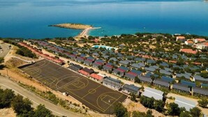 Vista aérea de una zona residencial costera con casas, una cancha deportiva y una masa de agua.