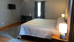 Ein Schlafzimmer mit einem Bett, einem Schreibtisch, einem Sessel, einem Deckenventilator und einem an der Wand befestigten Fernseher.