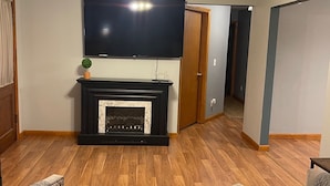 Ein Wohnzimmer mit Kamin, einem an der Wand befestigten Fernseher und einem Deckenventilator.
