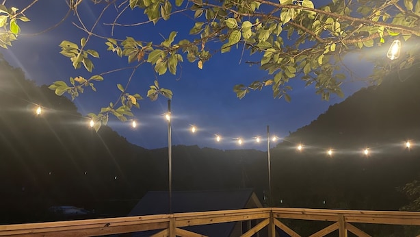Ein Whirlpool mit Holzterrasse und Lichterkette, umgeben von Bäumen und einer Berglandschaft.