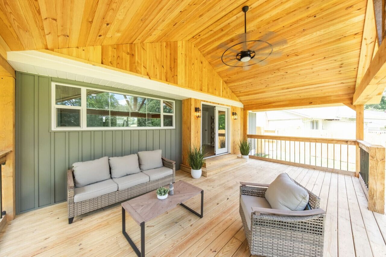 A covered porch with a wicker sofa, a coffee table, and a wicker chair.