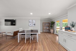 A modern kitchen with white cabinetry, a dining area with a wooden table and chairs, and a large window providing natural light. - Lakeview Retreat | Family-Friendly · Near Downtown (Macon)