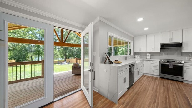 A modern kitchen with white cabinets, a built-in oven, and a large window overlooking a deck. - Lakeview Retreat | Family-Friendly · Near Downtown (Macon)