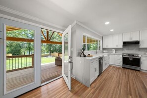 Una cucina moderna con mobili bianchi, forno integrato e un'ampia finestra vista su un patio.