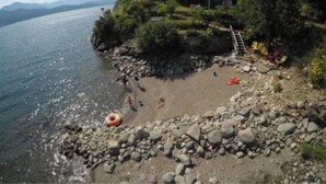 A house on a rocky shore with a clear view of the lake and mountains in the background. - Vacation Home For Rent - Ainsworth BC (Ainsworth)