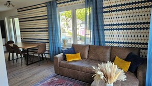 Ein Wohnzimmer mit einem braunen Sofa, gelben Kissen, einem gemusterten Teppich und einer Vase mit Trockenblumen.