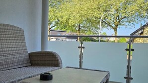 Ein Korbssessel und ein kleiner Tisch auf einem Balkon mit Blick auf Bäume und Häuser.