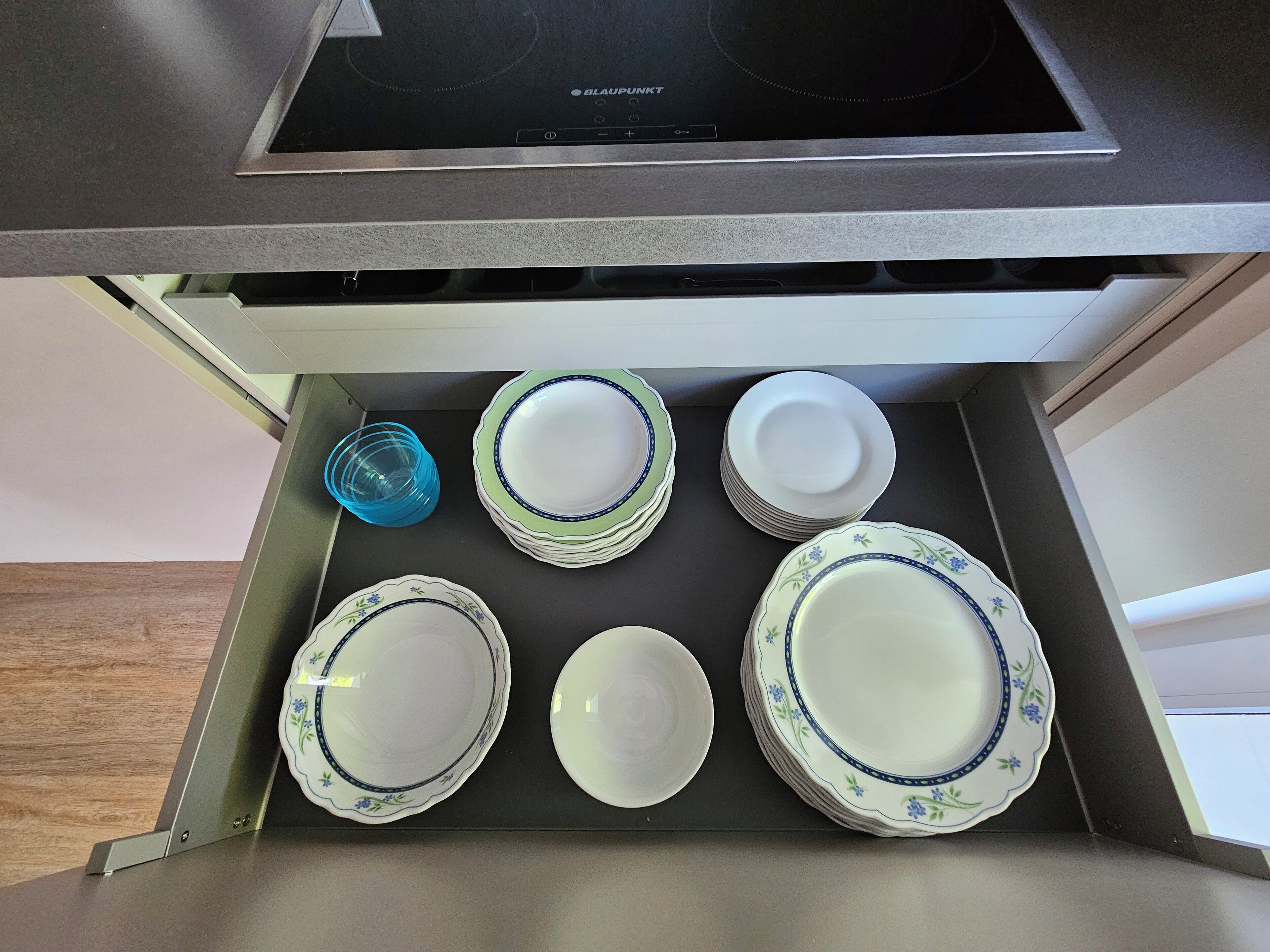 A kitchen drawer with a stack of plates and a blue glass container.