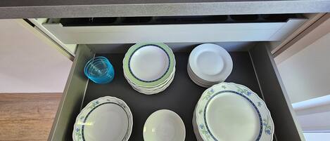 A kitchen drawer with a stack of plates and a blue glass container.