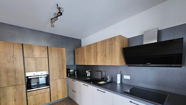 Eine moderne Küche mit Holzausstattung, einem Einbauofen, einer schwarzen Dunstabzugshaube und einer Spüle aus Edelstahl.