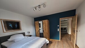 Ein Schlafzimmer mit einem Bett, einem Nachttisch, einem Holzschrank und einer Tür zu einem anderen Raum.