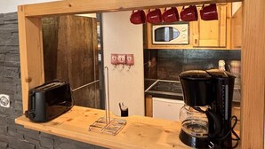 A kitchen with a wooden countertop, a microwave, a stove, and hanging mugs.