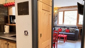 A kitchen with wooden cabinets, a sign reading "Cuisine", and a dining area with a red table and chairs.