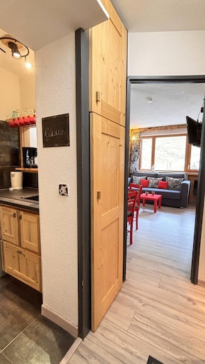 Uma cozinha com armários de madeira, uma placa com a palavra 'Cuisine' e um espa ço de jantar com uma mesa e cadeiras vermelhas.