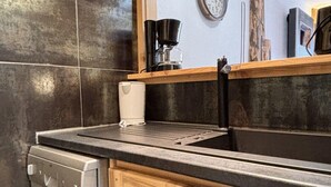 A kitchen with a dishwasher, wooden cabinets, a black countertop, and a wooden shelf with red mugs.